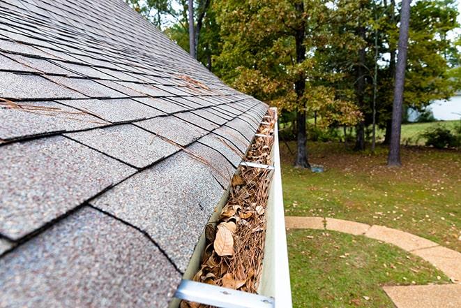 man clearing leaves and debris from a clogged gutter